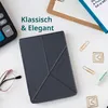 A dark gray e-reader cover is displayed on a white surface with office supplies like a calculator, glasses, and paper clips. Náhľad obrázku produktu
