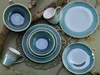 A collection of ceramic tableware, including bowls, plates, and mugs, arranged on a green surface with natural elements like branches and catkins. Náhľad obrázku produktu