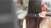 A woman is using an electric hair straightening brush on her long, dark hair. Produktbild-Vorschau
