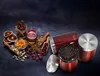 A collection of ingredients for beverages, including tea, coffee, cinnamon, dried oranges, honey, and rosebuds, arranged around red storage containers. Voir les images du produit