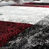 A close-up, low-angle view of a rug with a geometric pattern of red, black, white, and gray squares. Voir les images du produit