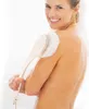 A woman is using a long-handled brush to exfoliate her back in a shower. Produktbild-Vorschau