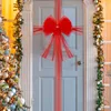 A decorated door with a large red bow and Christmas garland, next to a Christmas tree. Náhled obrázku produktu