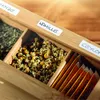 A close-up view of a wooden tea box filled with various types of tea, including loose leaf and tea bags. Produktbild-Vorschau