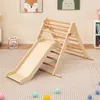 A wooden climbing triangle with a slide, set up on a carpeted floor in a room with children's artwork on the wall. Produktbild-Vorschau