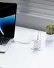 A white laptop is charging via a white power adapter plugged into a white wall socket. A small cactus in a white pot sits to the right. Produktbild-Vorschau