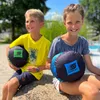 Two children are sitting on a rock outdoors, each holding a round, soft object. A swimming pool is visible in the background. Produktbild-Vorschau