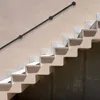 A black handrail runs diagonally across a light beige wall, attached to a set of concrete stairs. Náhled obrázku produktu