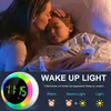 A mother kissing her sleeping daughter goodnight, with a wake-up light alarm clock in the foreground. Produktbild-Vorschau