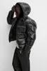 A person wearing a black puffer jacket and dark pants, posing against a light gray background. Produktbild-Vorschau