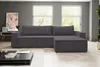 A dark gray sectional sofa with a chaise lounge is shown in a modern living room setting with large windows and a coffee table in the foreground. Produktbild-Vorschau