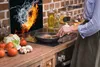 A person is cooking in a kitchen with a glass splashback showing fire and water. Produktbild-Vorschau