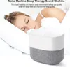 A woman sleeping in bed next to a white and gray sound machine. Produktbild-Vorschau