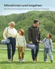 A family is walking in a grassy field with trees in the background, carrying picnic blankets. Produktbild-Vorschau