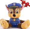 A plush toy of Chase from Paw Patrol wearing a festive sweater and hat, with a red ribbon overlay. Produktbild-Vorschau