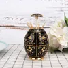 A decorative black and gold toothpick holder sits on a checkered tablecloth, with white flowers in the background. Náhled obrázku produktu