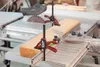 Two red and black clamps are holding a wooden plank on a table saw. Podgląd zdjęcia produktu