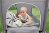 A baby playing in a portable crib with toys and a stuffed animal. Podgląd zdjęcia produktu