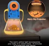 A baby projector lamp is shown in use, projecting stars and a moon onto a surface, with a baby sleeping in the background. Produktbild-Vorschau