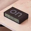 A black digital alarm clock with the word "on" on its surface sits on a marble-like surface. Podgląd zdjęcia produktu