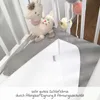 A baby crib with a stuffed llama toy and a white and gray polka dot blanket. Produktbild-Vorschau