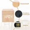 A close-up marketing image of a wooden cube alarm clock with digital display, showing details of its material, controls, and battery compartment. Produktbild-Vorschau