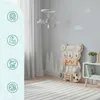 A Montessori busy board shaped like a bear is displayed in a child's room, next to a shelf with books and a plant. The room has light gray walls with cloud and tree decals, and a striped rug on the floor. Produktbild-Vorschau