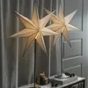 Two star-shaped lamps are displayed on a table with a gift and pinecones, in front of a curtain. Podgląd zdjęcia produktu