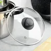 A close-up of a glass pot lid with a black handle and a stainless steel rim, resting on a light gray surface. Podgląd zdjęcia produktu