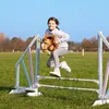 A young girl is jumping over a hurdle on a hobby horse in a grassy field. Anteprima dell’immagine prodotto