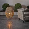 An outdoor patio scene with a wicker lamp and furniture. Produktbild-Vorschau