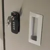 A close-up view of a stainless steel locker door with a combination lock and a key inserted, alongside a recessed handle. Anteprima dell’immagine prodotto