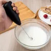 A hand holding a black milk frother over a bowl of frothed milk. Produktbild-Vorschau