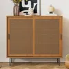 A wooden sideboard with cane doors sits on a wooden floor in front of a white wall. Decorative items are placed on top of the sideboard. Produktbild-Vorschau