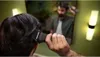 A person is trimming their hair in front of a mirror, with two lamps visible in the background. Produktbild-Vorschau