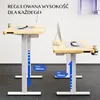 Two adjustable height desks are shown side-by-side on a carpeted floor, against a white wall with some shelving visible in the background. Podgląd zdjęcia produktu