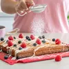 A person is dusting powdered sugar onto a cake decorated with berries. Produktbild-Vorschau