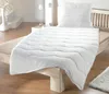 A white duvet and pillow set laid out on a wooden bed frame in a bright, minimalist bedroom. Produktbild-Vorschau