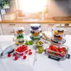 A collection of glass food storage containers filled with various fruits and vegetables, arranged on a marble countertop in a kitchen setting. Produktbild-Vorschau