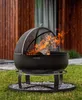 A fire pit with flames burning in a grassy outdoor setting with a wooden building in the background. Produktbild-Vorschau
