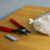 A close-up shot of a food netting tool and a roll of netting on a wooden cutting board. Produktbild-Vorschau