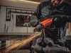 A man is using an angle grinder to cut a metal pipe in a workshop. Podgląd zdjęcia produktu