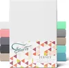 A stack of folded jersey fitted sheets in various colors, with a white sheet prominently displayed in the foreground. Produktbild-Vorschau