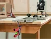 A woodworking clamp is attached to a workbench, holding a router and a track guide in place. Podgląd zdjęcia produktu