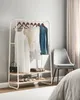 A white garment rack with clothes hanging on it, a chair next to it, and a bed in the foreground. Náhled obrázku produktu