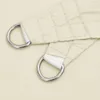 Close-up of the corner of a cream-colored sail shade, showing the D-ring attachment. Produktbild-Vorschau