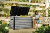 A woman is reading a book while sitting on a bench next to a large storage box on a patio surrounded by plants. Produktbild-Vorschau