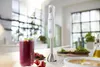 A white immersion blender is shown on a kitchen counter next to a glass of berry smoothie and a bowl of salad. Voir les images du produit