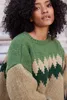A close-up shot of a woman wearing a knitted sweater. Produktbild-Vorschau