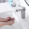 A person is washing their hands under a modern waterfall faucet in a bathroom sink. Produktbild-Vorschau